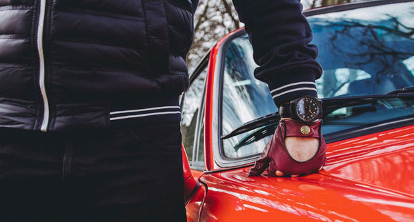 A person leaning on a car wearing a GRD watch and a pair of gloves