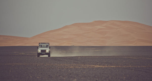 A Land Rover crossing a plain in Africa with a sand dune in the background