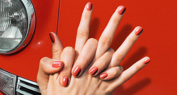 A pair of hands with red nail varnished matched to the front of a classic red Porsche
