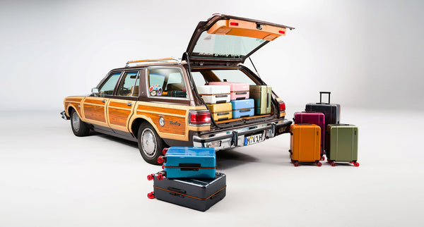 A studio photo of a family estate car with the boot open and a selection of Floyd suitcases around it