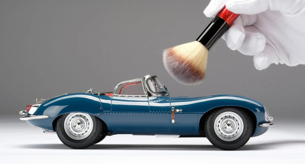 A studio shot of a scale model of a Jaguar XKSS with a hand holding a brush to clean the car